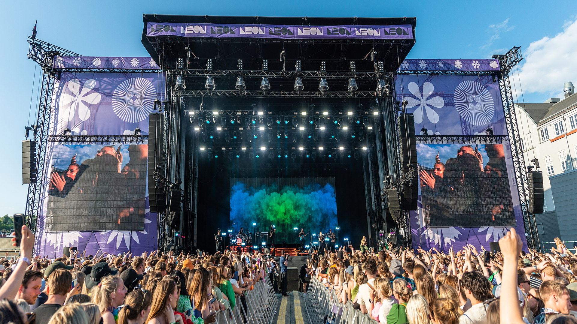 The NEON festival stage with purple branding, suspended PA arrays and a daylight audience.